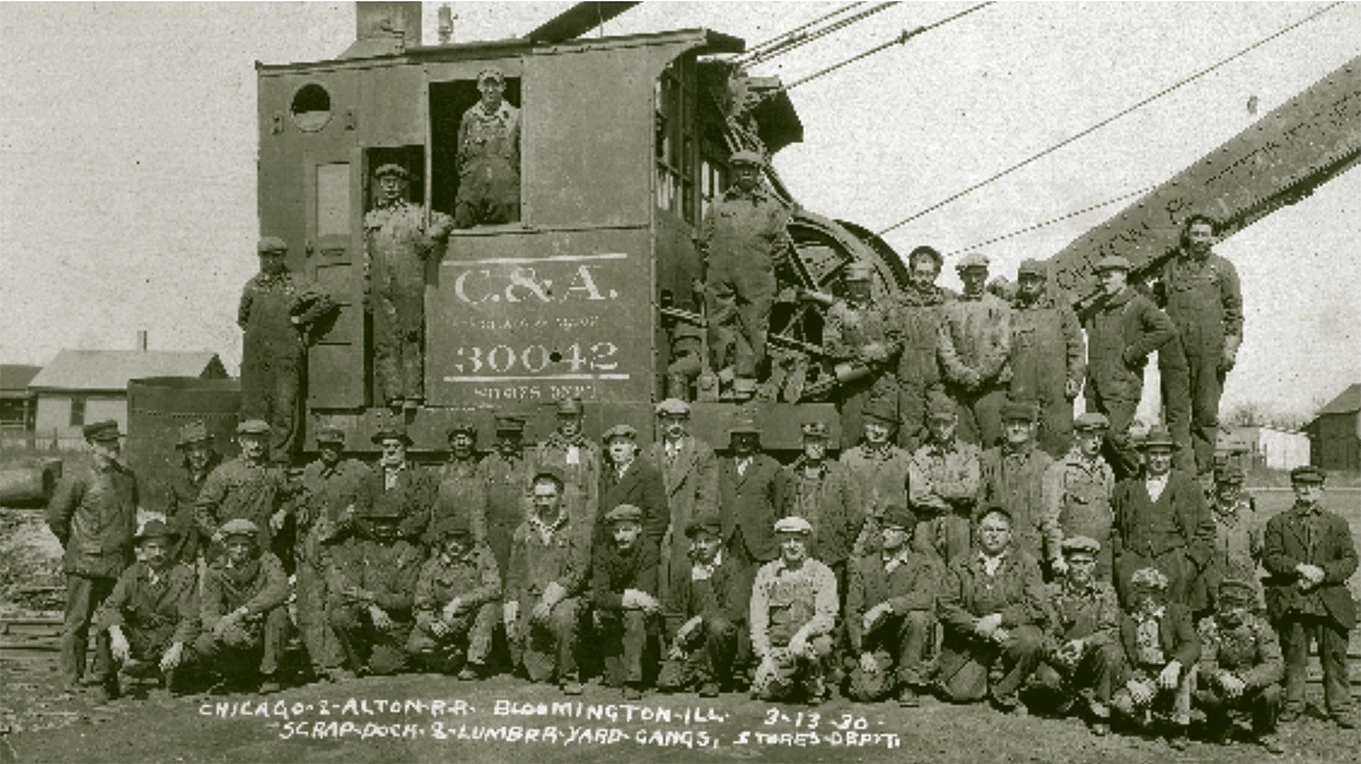 A group photograph of approximately 40 people posing for a group photo outdoors on a large piece of equipment, possibly a crane.