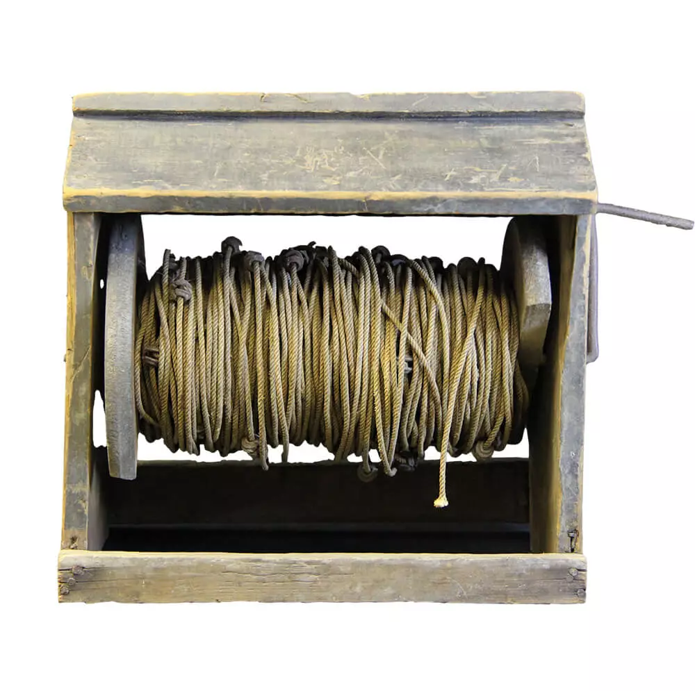 A wooden box with a gable top that contains a spool of cable and a handle to wind it. The cable has knots and little metal pieces.