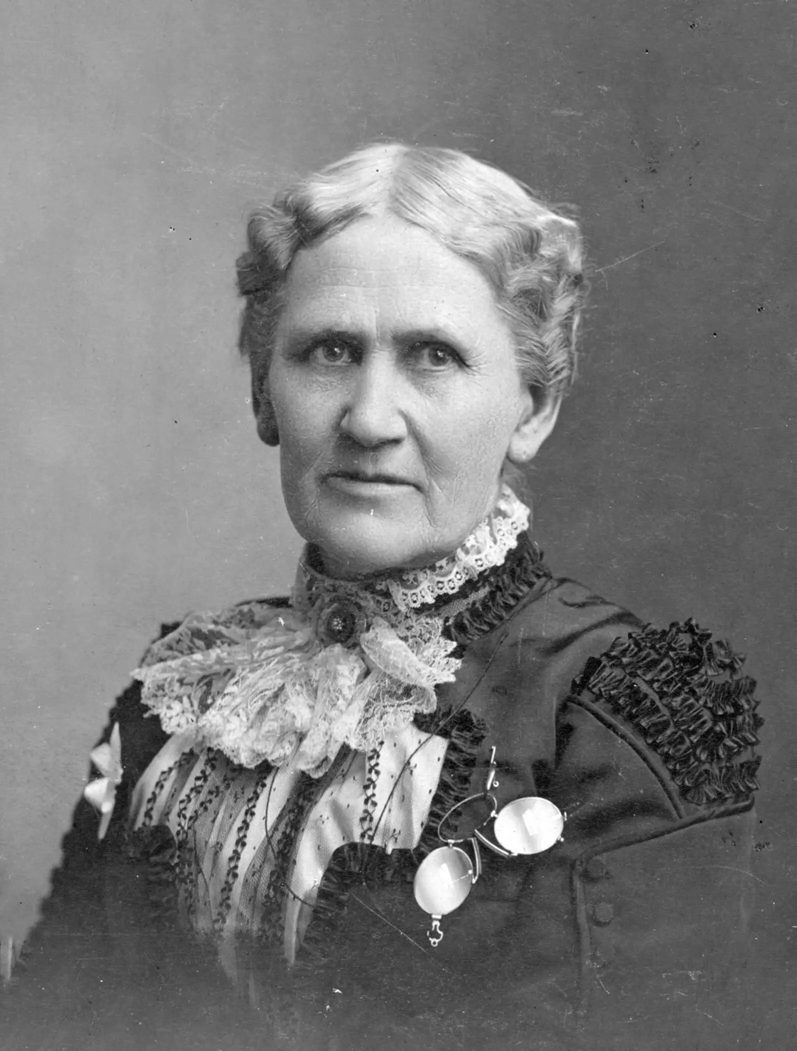Black and white portrait of an older white woman in an ornate dress, white hair pulled back