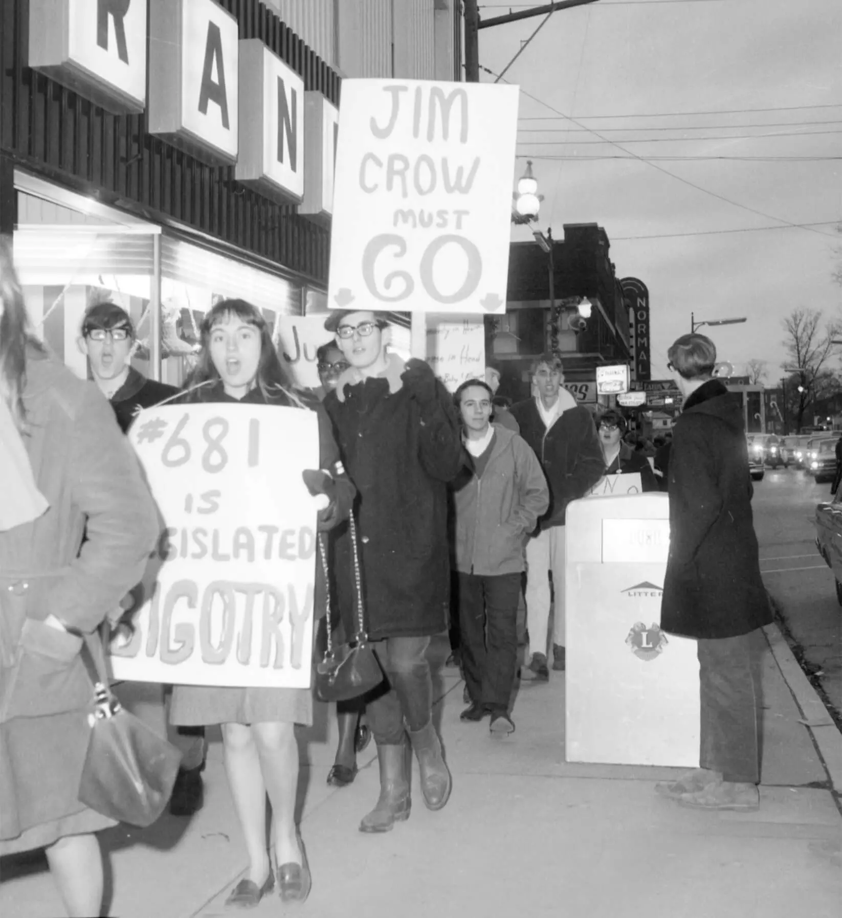 Black and white photo of college students protesting on a city sidewalk. They are holding up signs standing against Jim Crow laws.