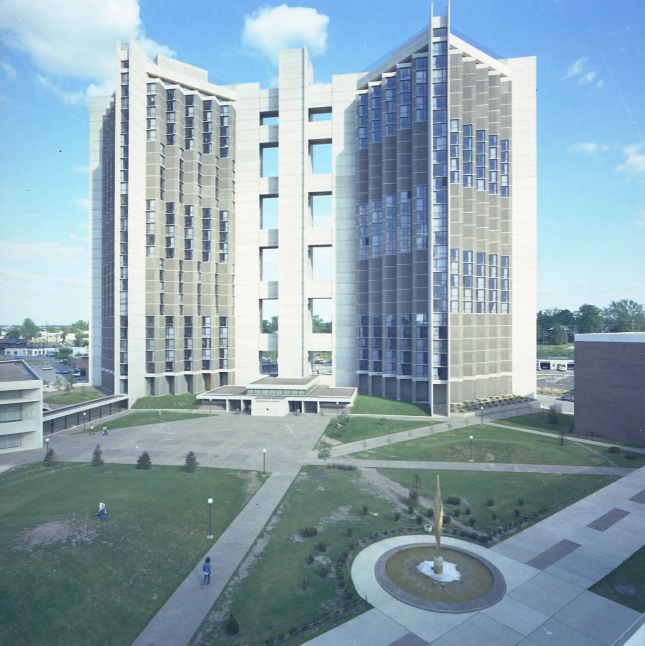Color photograph of the 40+ story brutalist style student housing building and the green space in front of it.