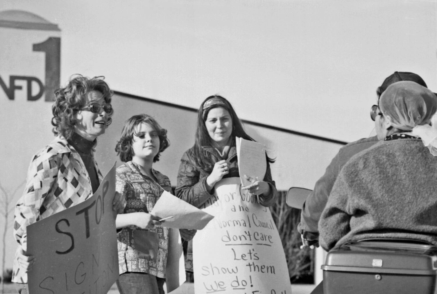 Black and white photo of four women holding poster board signs in front of a building.