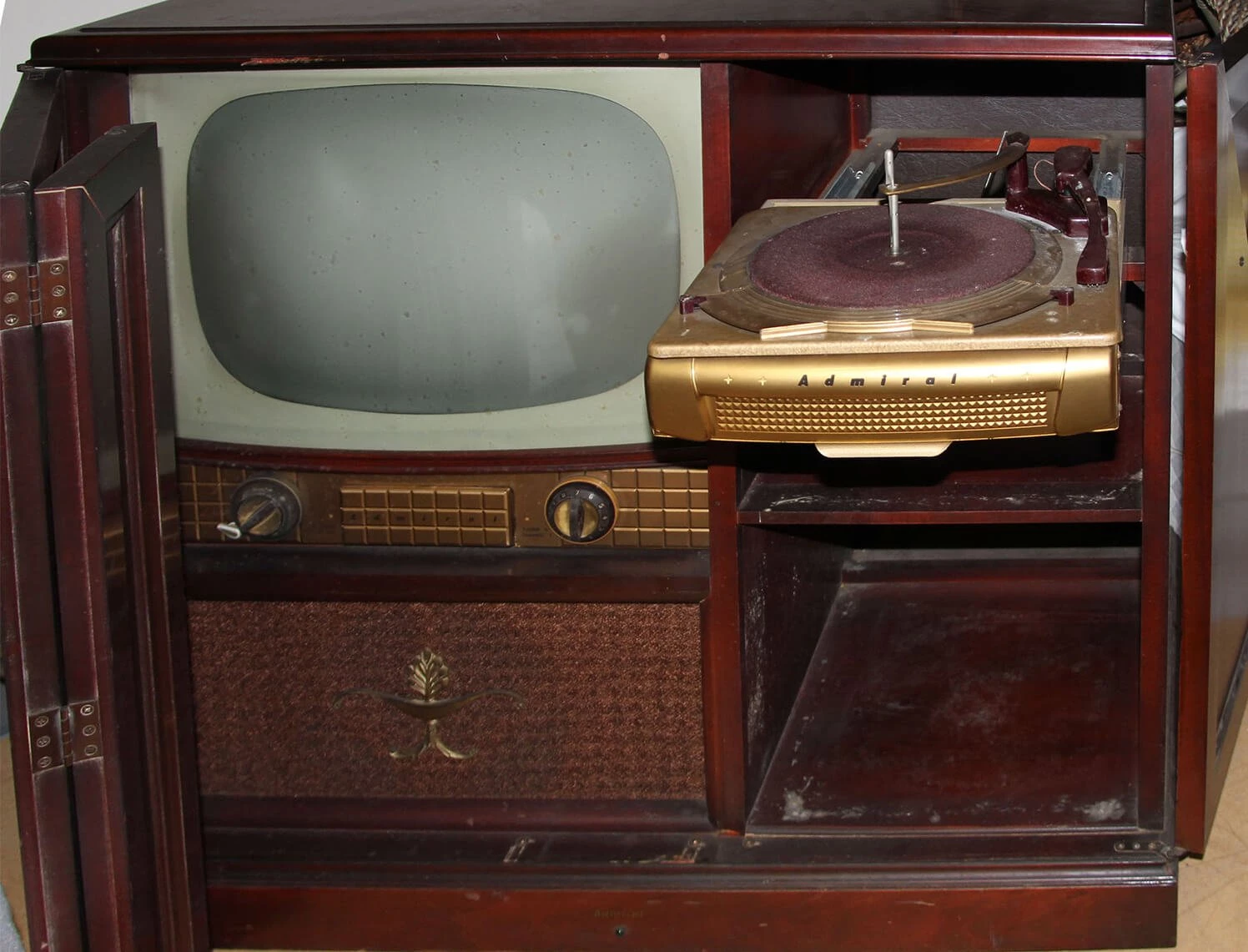 Photo of a console television with its door open.  There is dust on the shelf.