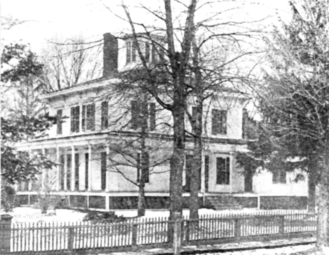 Black and white photograph of the Fell home, two stories with a cupola. The house appears to be white, fenced in and surrounded by trees.
