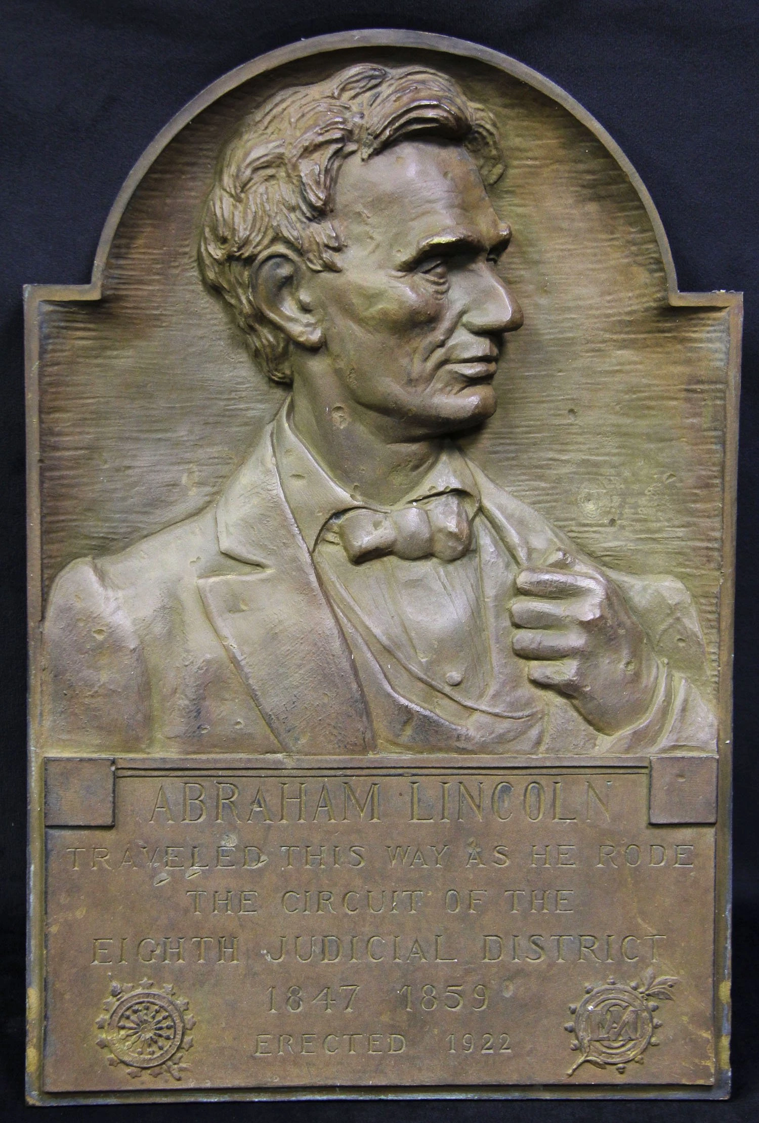 A bronze bas-relief sculpture of the right profile of Abraham Lincoln's face. He is looking to the left, and his left hand is tucked around, holding the collar of his jacket. Below the depiction of Lincoln reads abraham lincoln traveled this way as he rode the circuit of 8th judicial district 1847 1859. erected 1922