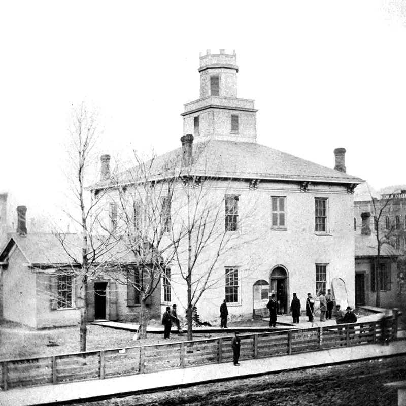Two story courthouse with a large cupola and men gathered out front.