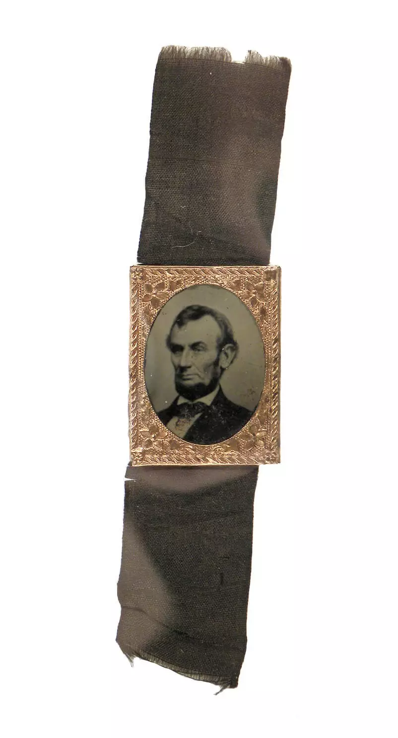 Dark ribbon with black and white photo of Lincoln in the center, surrounded by small, ornate brass frame.