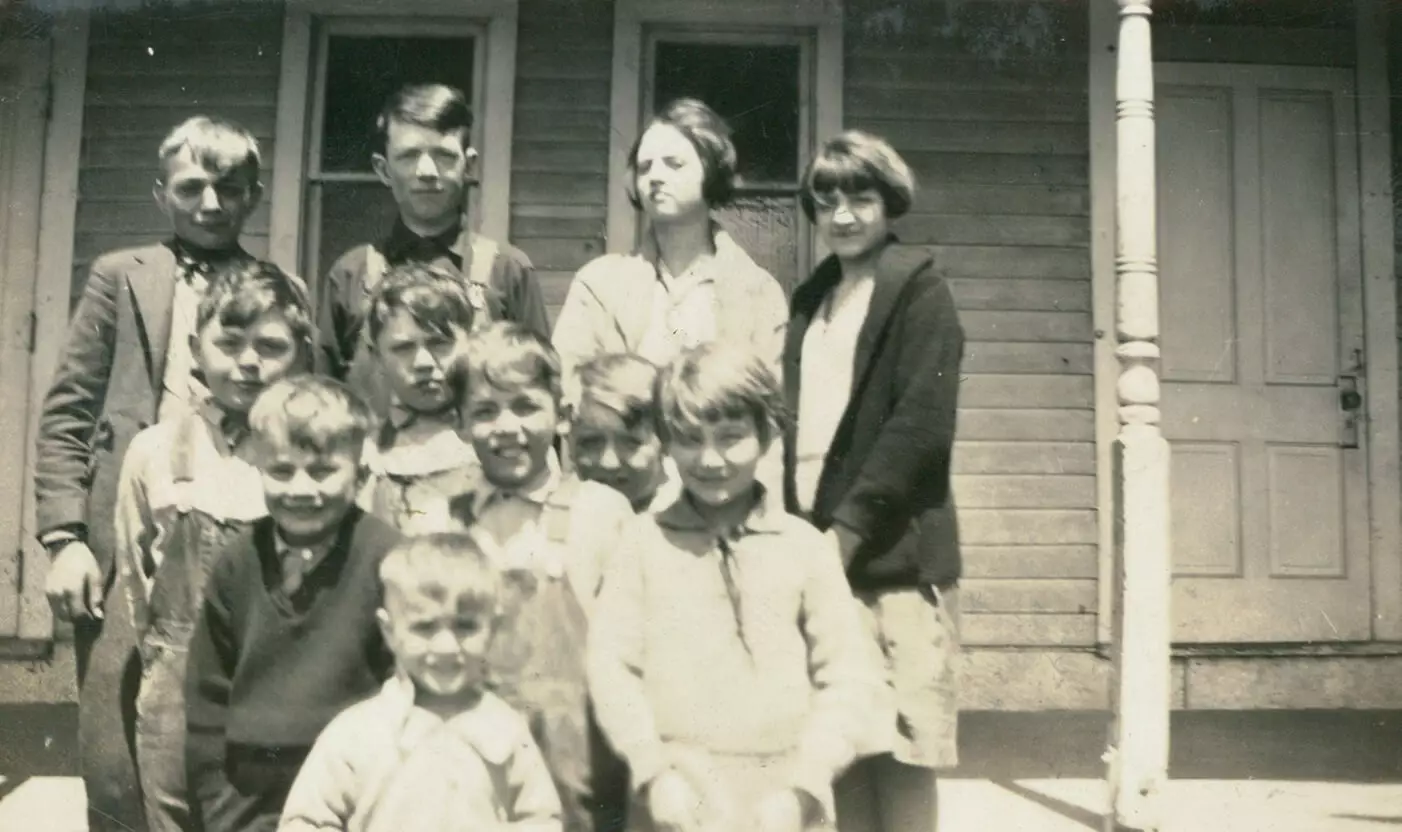 Black and white photo of ten young children in front of a porch