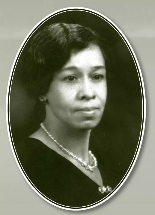 Portrait of an African American woman with her hair pulled back. she is wearing a pearl necklace and a shirt or dress with a v-neckline and brooch.