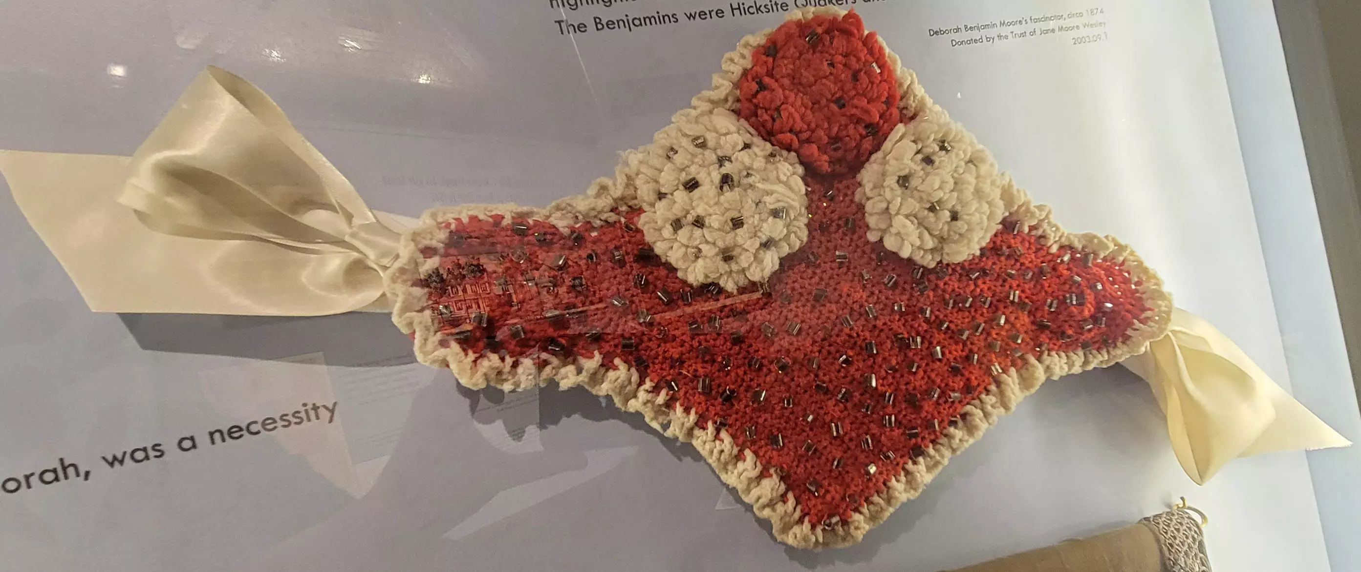 Photo of a knitted red and beige diamond-shaped accessory filled with padding, with ribbons at both ends.