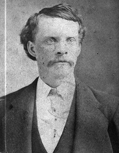 Grainy black and white portrait of a light-skinned man wearing a suit and vest. His hair is medium length and combed to the side. He has a mustache.