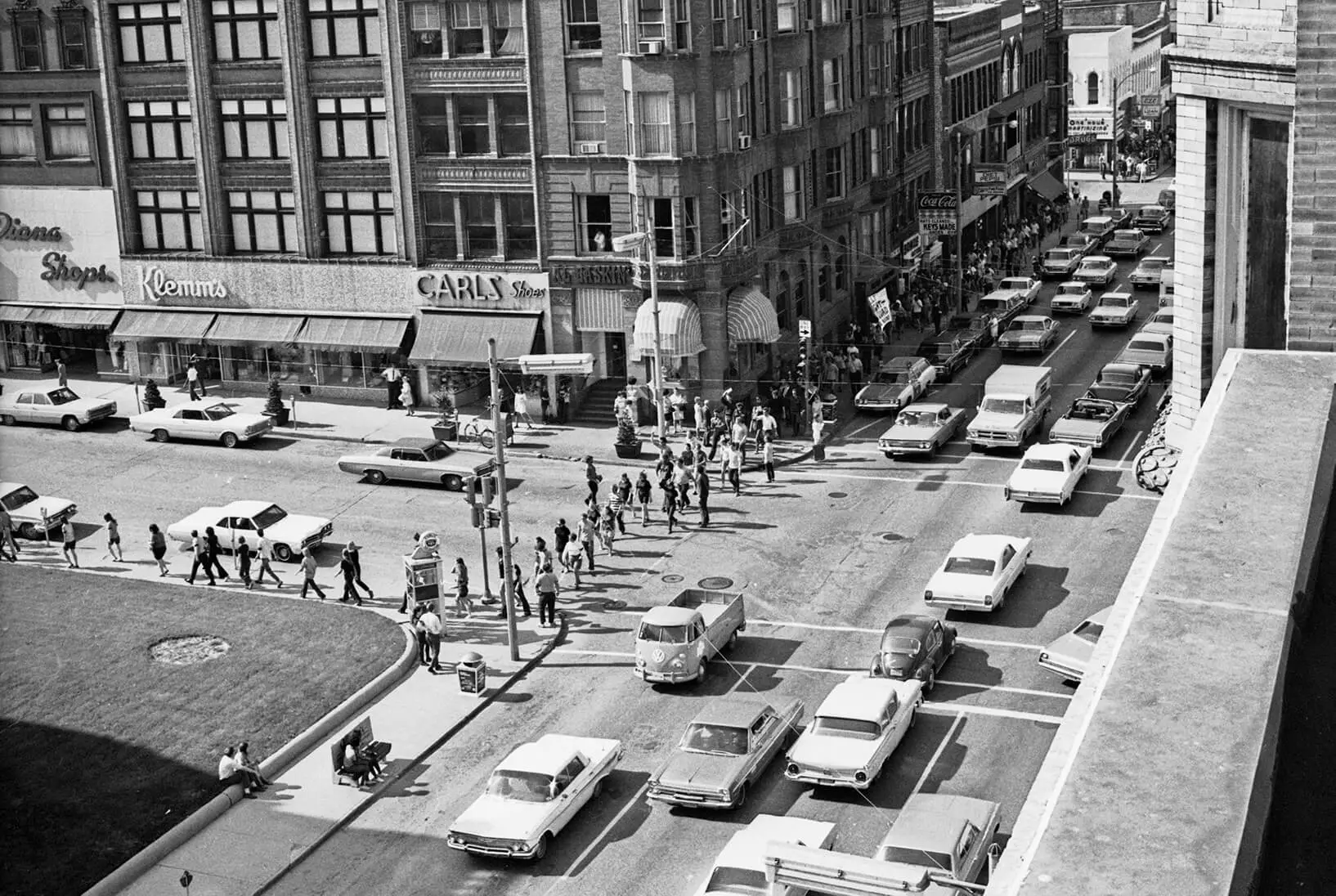 Photo taken from above of traffic and protesters, looking at the intersection of Jefferson and Main Streets. Bystanders not involved in the protest are observing from street benches. There are many cars on Main Street, traveling in both directions. Marchers can be seen as far as the eye can see on the sidewalk on Main St.