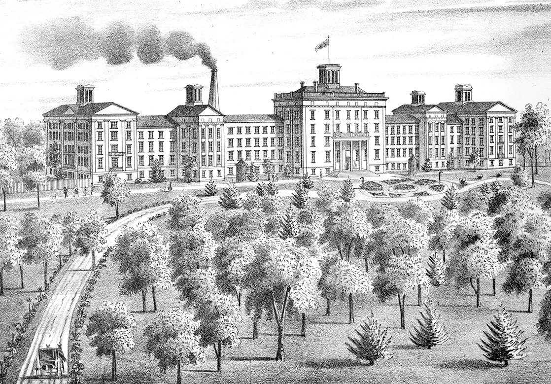 Large building with a smoking chimney and five cupolas. A long driveway winds through a field of trees.