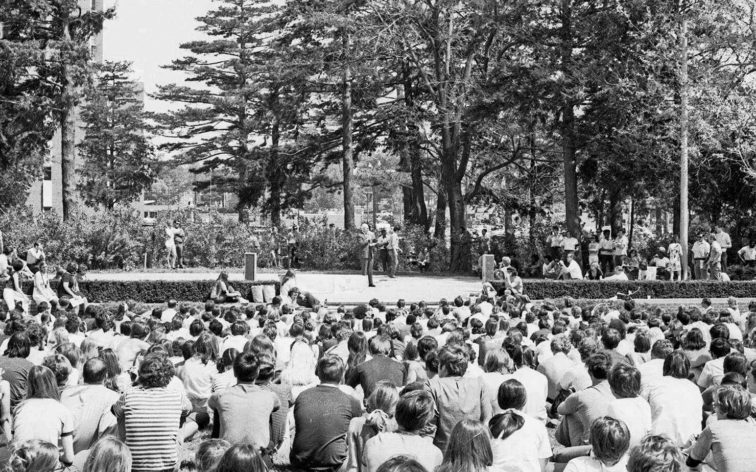 Middle-aged white man in a suit speaks to a group of hundreds of seated college students.
