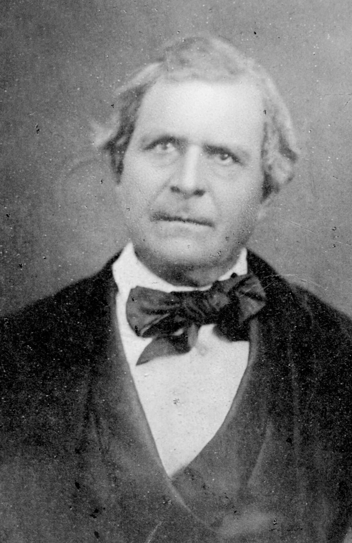 Black and white portrait of a middle-aged man with parted hair in a suit and bow tie.