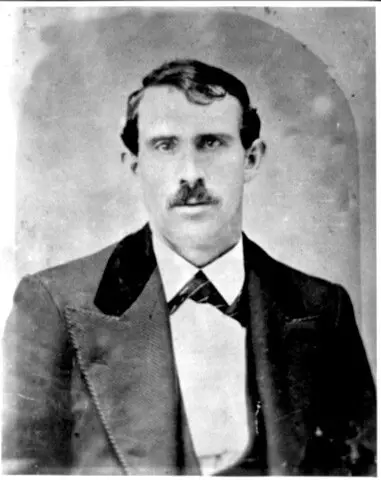 Black and white portrait of a man with wavy hair and a small cropped mustache, wearing a suit.