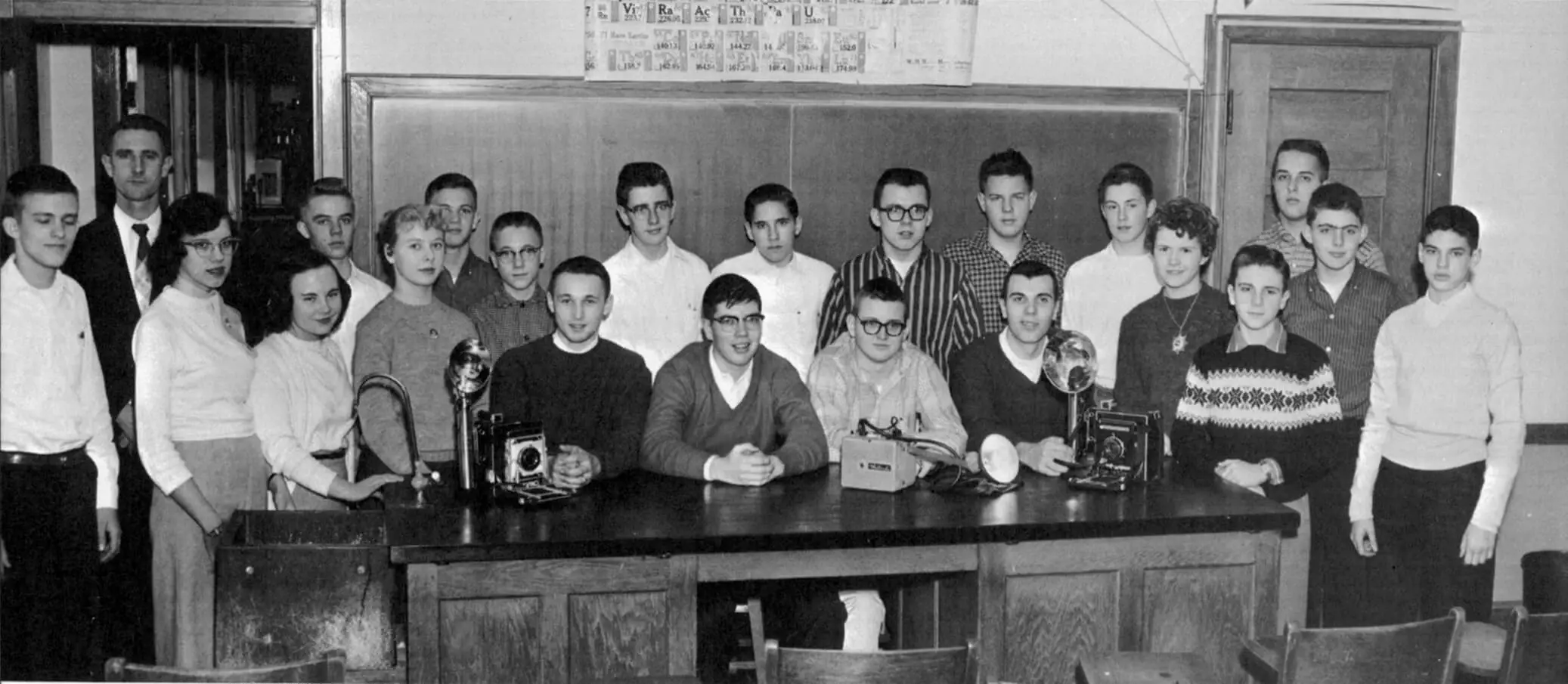 Black and white photo of a group of 22 young men and women in high school, as they pose with cameras.