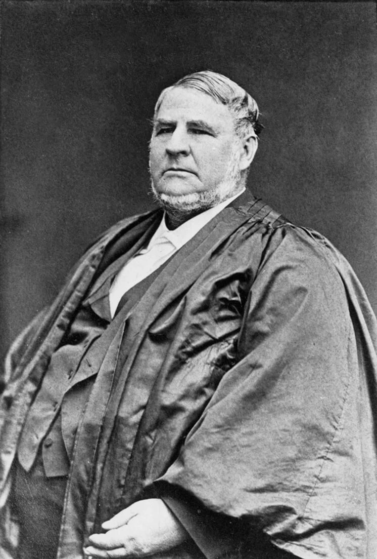 Black and photo of large bearded man in judge’s cloak.