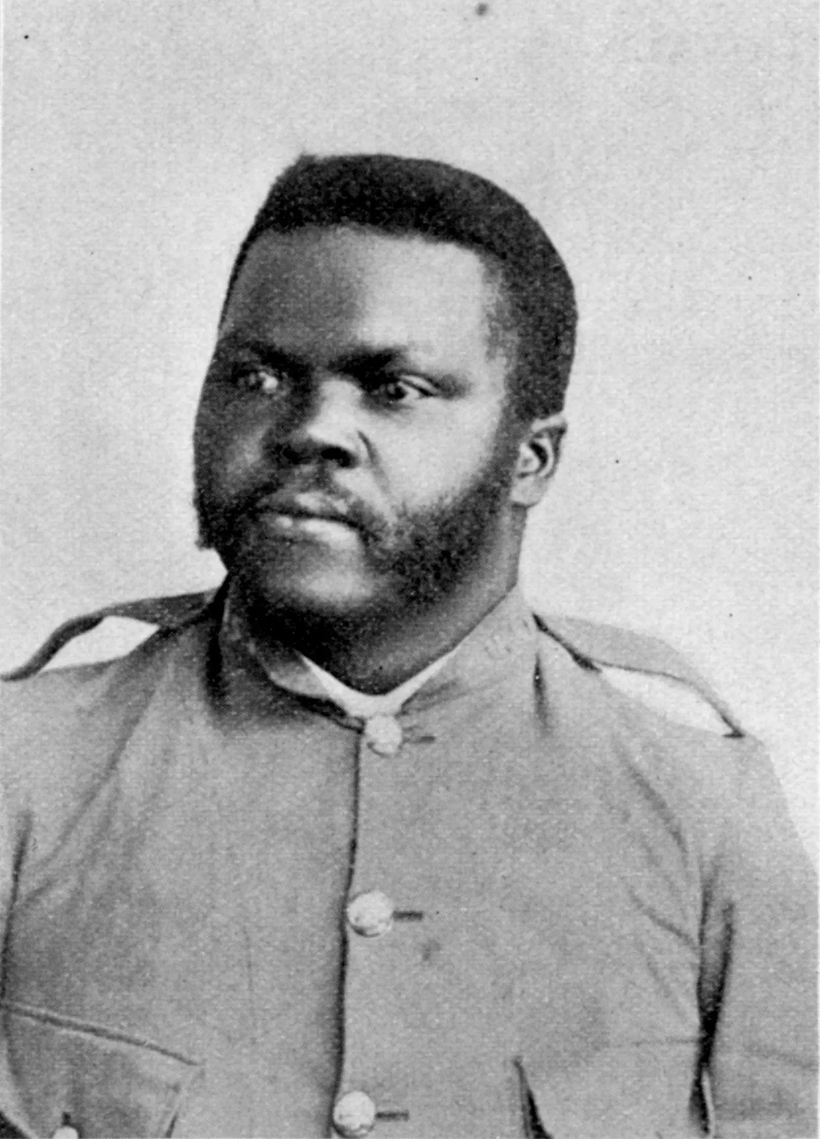 Black and white portrait of a young Black man in uniform. He has short black hair and a trimmed black beard and mustache.