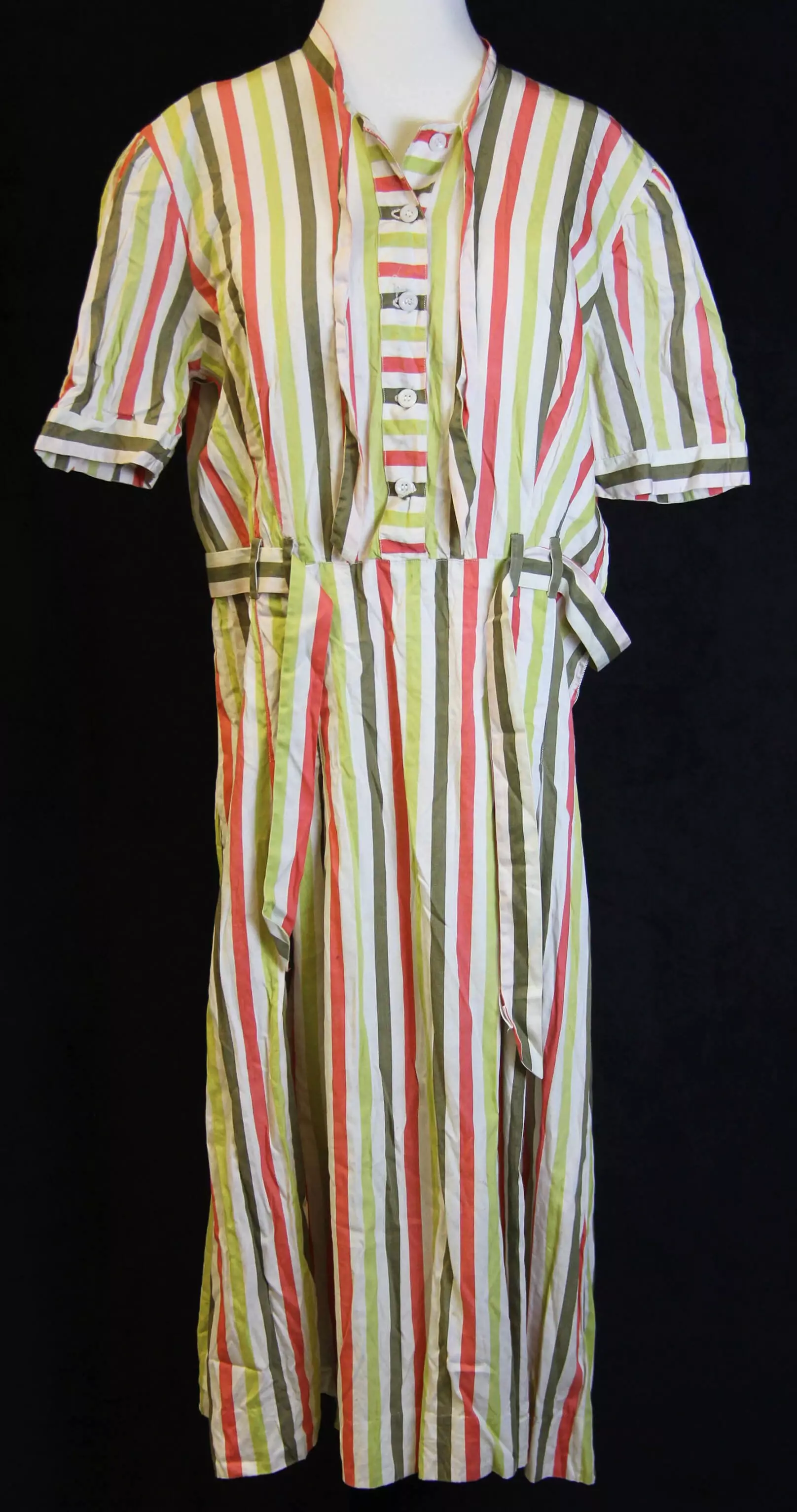 Color photo of a dress on a mannequin.  The dress has white, light green, orange, and dark green vertical stripes of equal width. The dress has 5 buttons above the waist, a built in belt of the same material around the waist, and short sleeves.