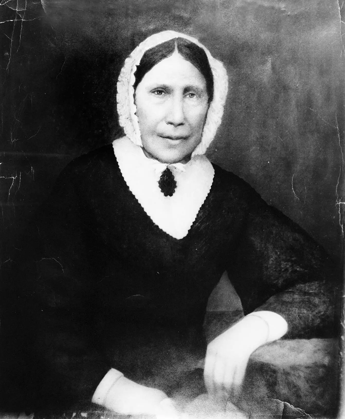 Portrait of a middle-aged light-skinned woman with dark hair, wearing a white bonnet and black dress.