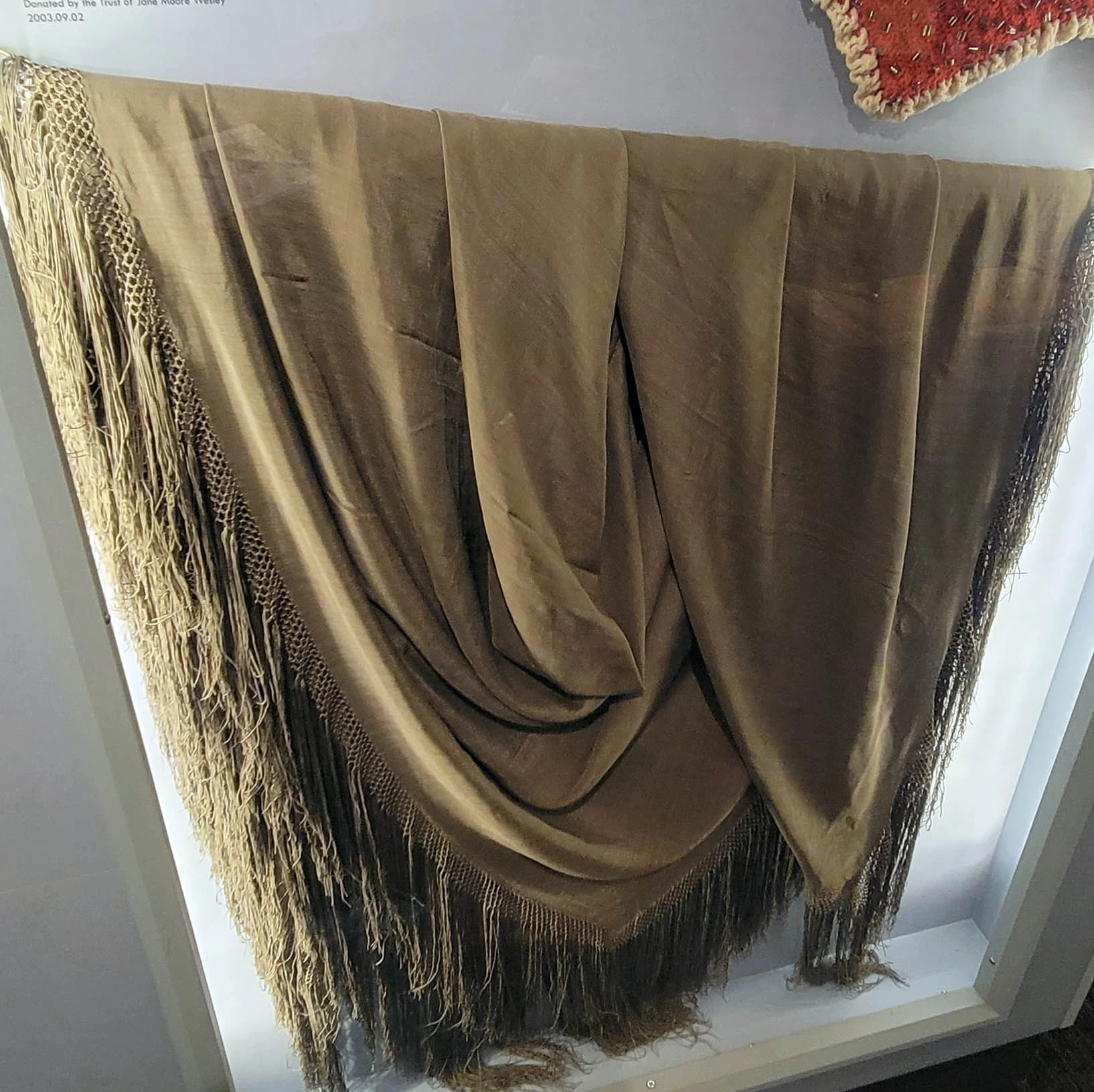 Photo of a beige fabric shawl with long fringe at the edges.