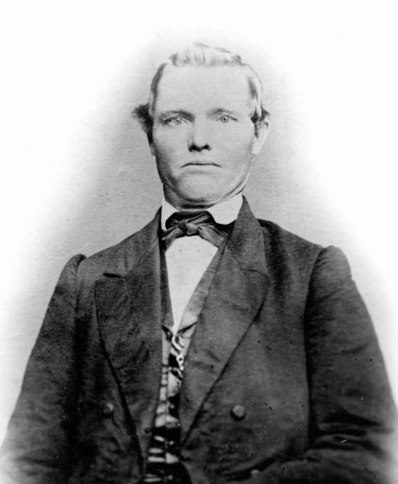 A white man in a three-piece suit and bow-tie poses for a portrait staring directly at the camera with a frown.