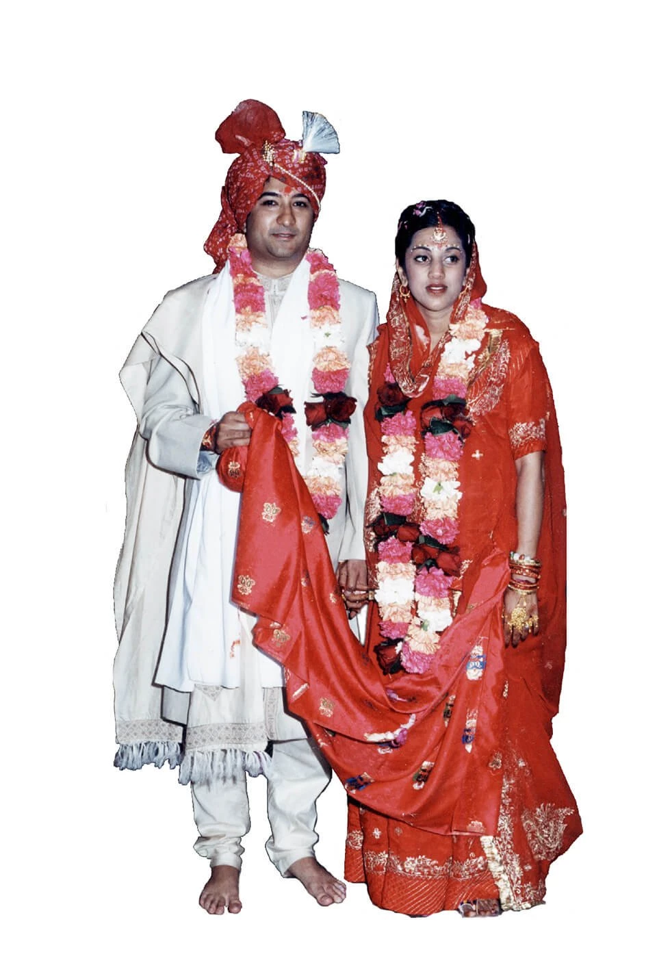 A picture of a couple standing together wearing traditional Indian clothing. The woman has a dress in red and the man is in white with a red head scarf.