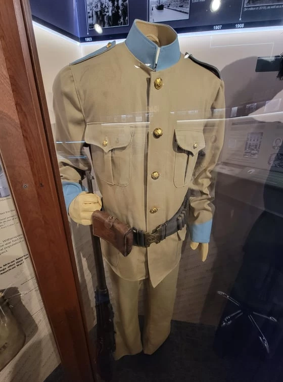 A beige colored uniform with blue collar and cuffs, brass buttons, and a leather utility belt with a pouch.