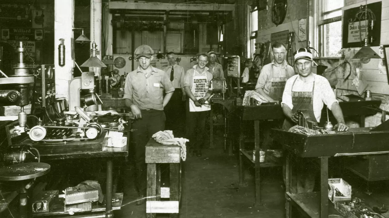 6 men stand in a workshop looking in the camera.