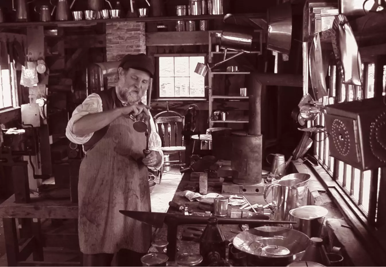 Man wearing an apron stands inside a workshop surrounded by tools and work surfaces