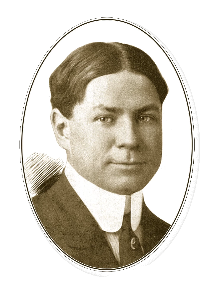 Portrait of a light-skinned man with medium length hair parted straight down the middle. He is wearing a dark suit jacket and tie, and his white collard shirt has a very tall collar.
